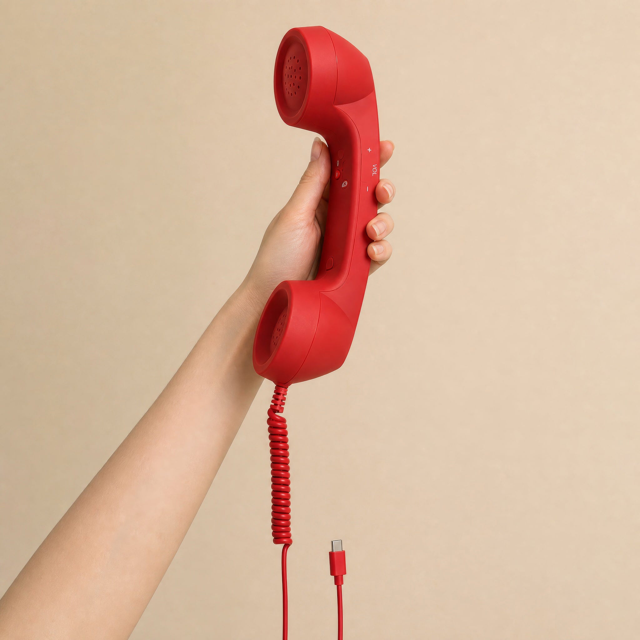 The red DialBoop Retro Handset held in one hand, for scale, cord and USB-C plug hanging below
