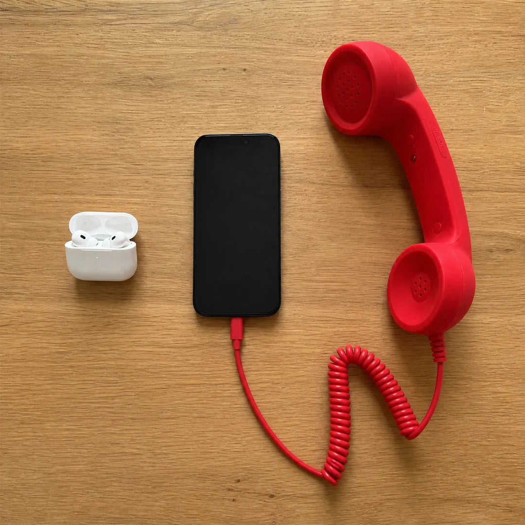 Wireless earbuds, a phone, and the red DialBoop handset laid out on an oak table