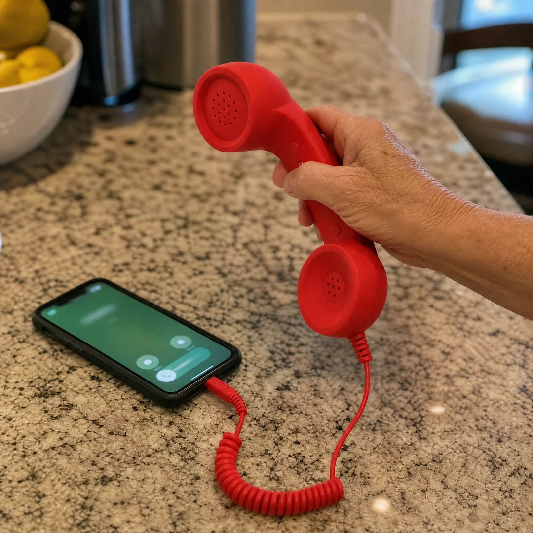 A hand reaches for the red DialBoop handset plugged into a ringing phone on a kitchen counter